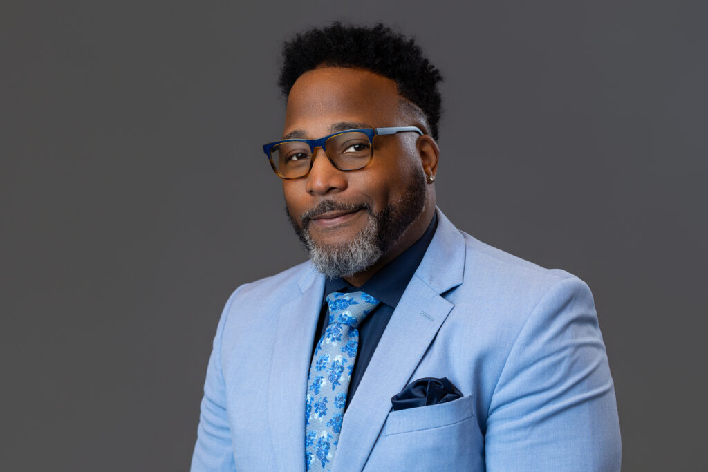 A man smiles at the camera in a professional headshot.